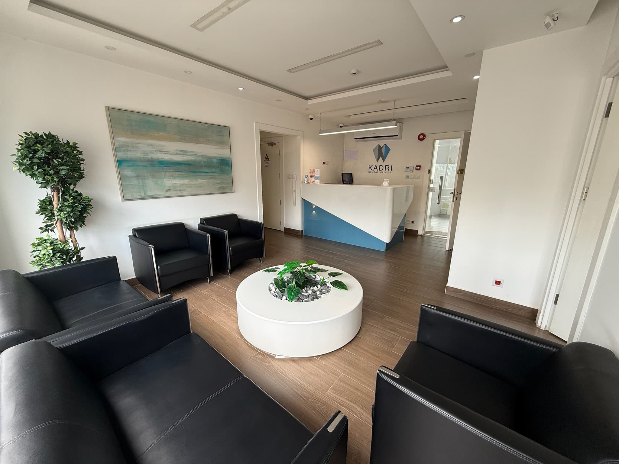 Modern dental clinic waiting room with black leather seating, white circular table, and reception desk.
