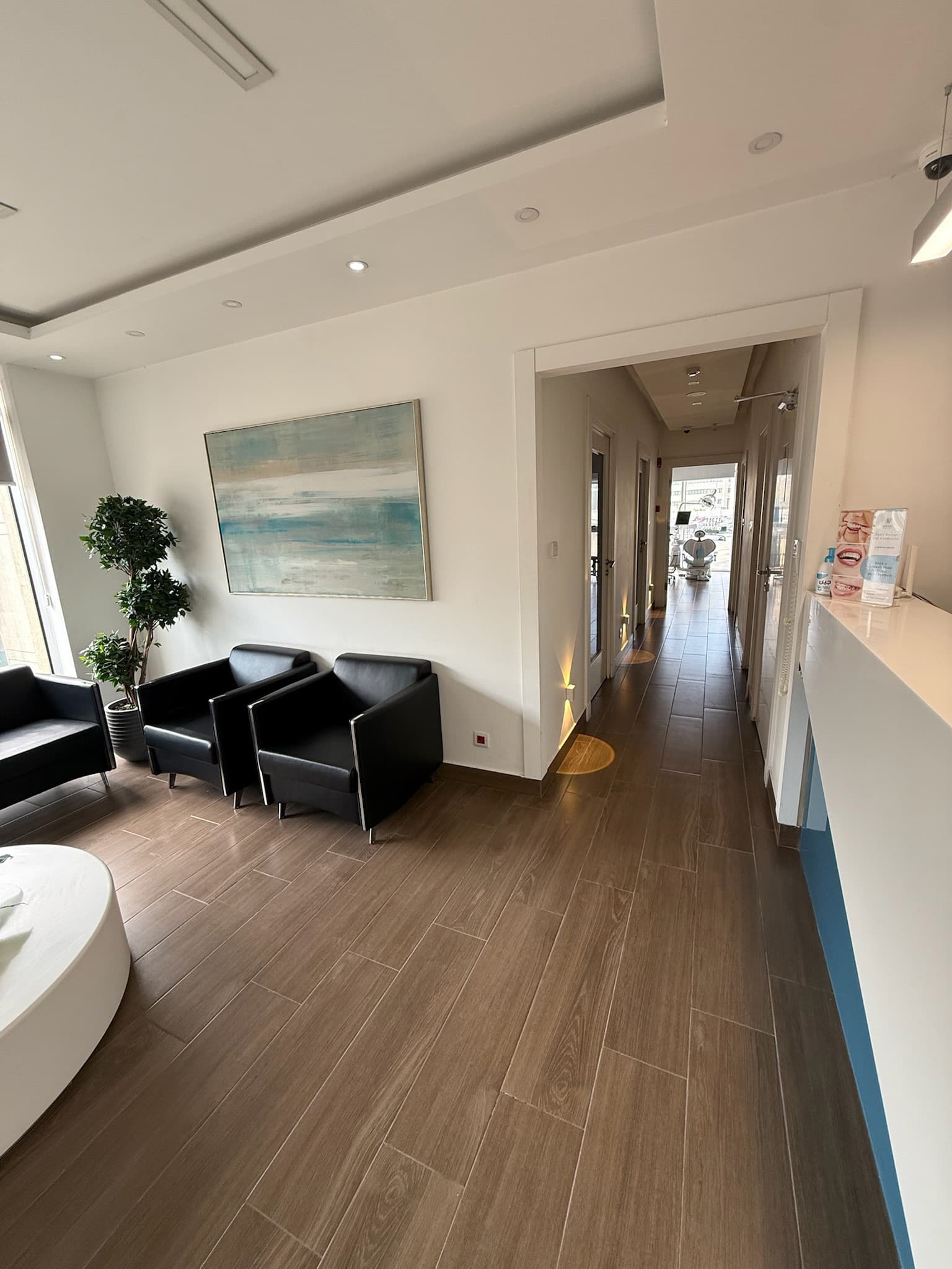 Modern dental clinic waiting room featuring black leather armchairs, abstract art, and a long hallway.